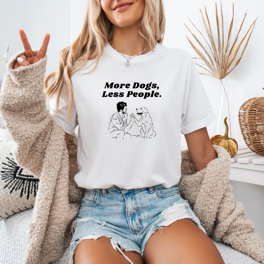 a woman sitting on a bed wearing a white shirt that says more dogs less people